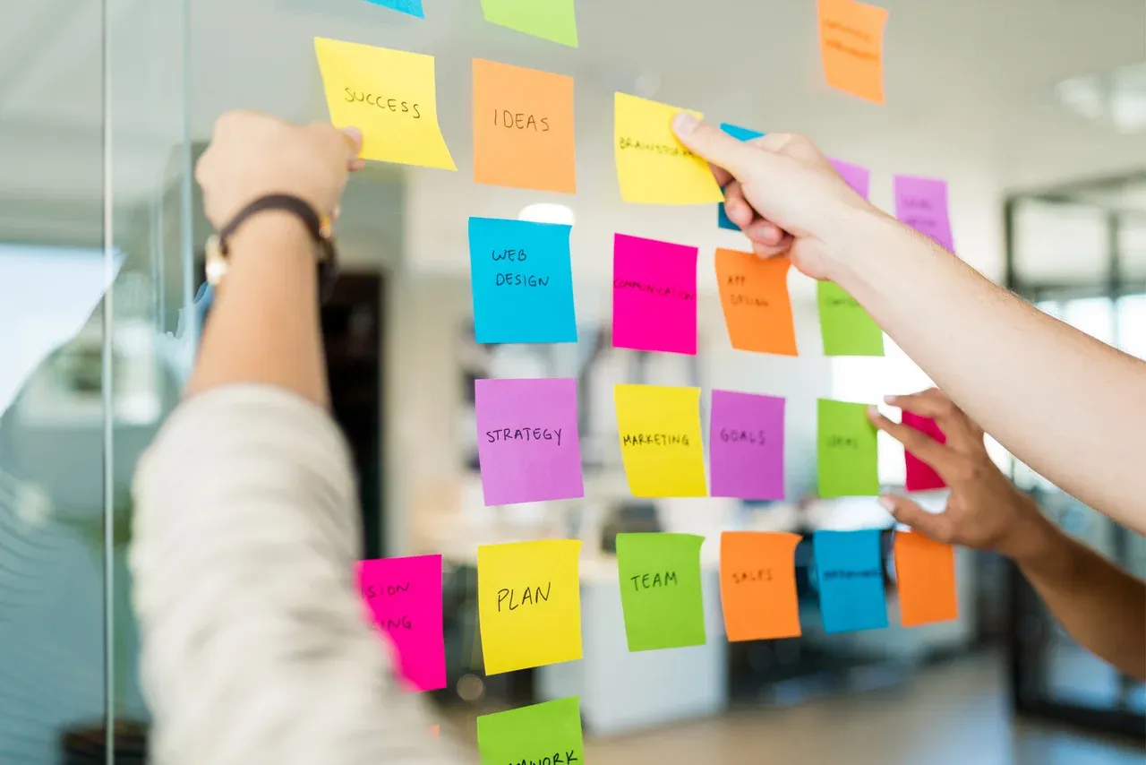 Team arranging sticky notes on glass in an office