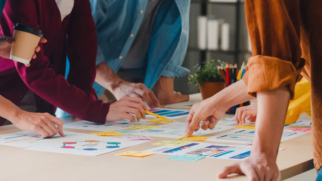 Team collaborating at a table with app wireframes, sticky notes, and a design-process diagram