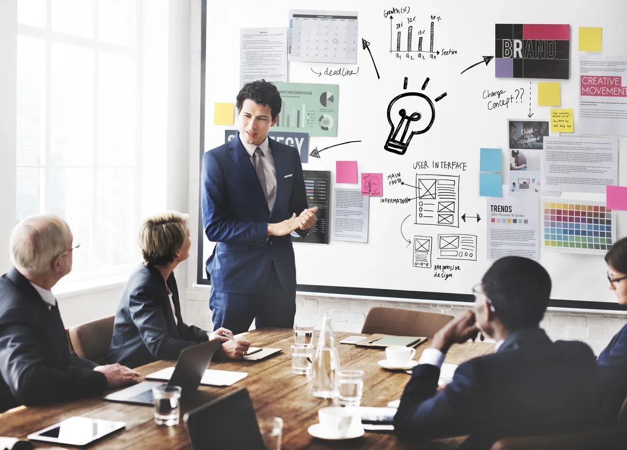 Presenter beside a whiteboard of UI sketches, brand notes, and sticky notes
